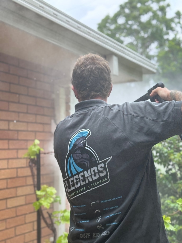 Worker pressure washing brick house exterior